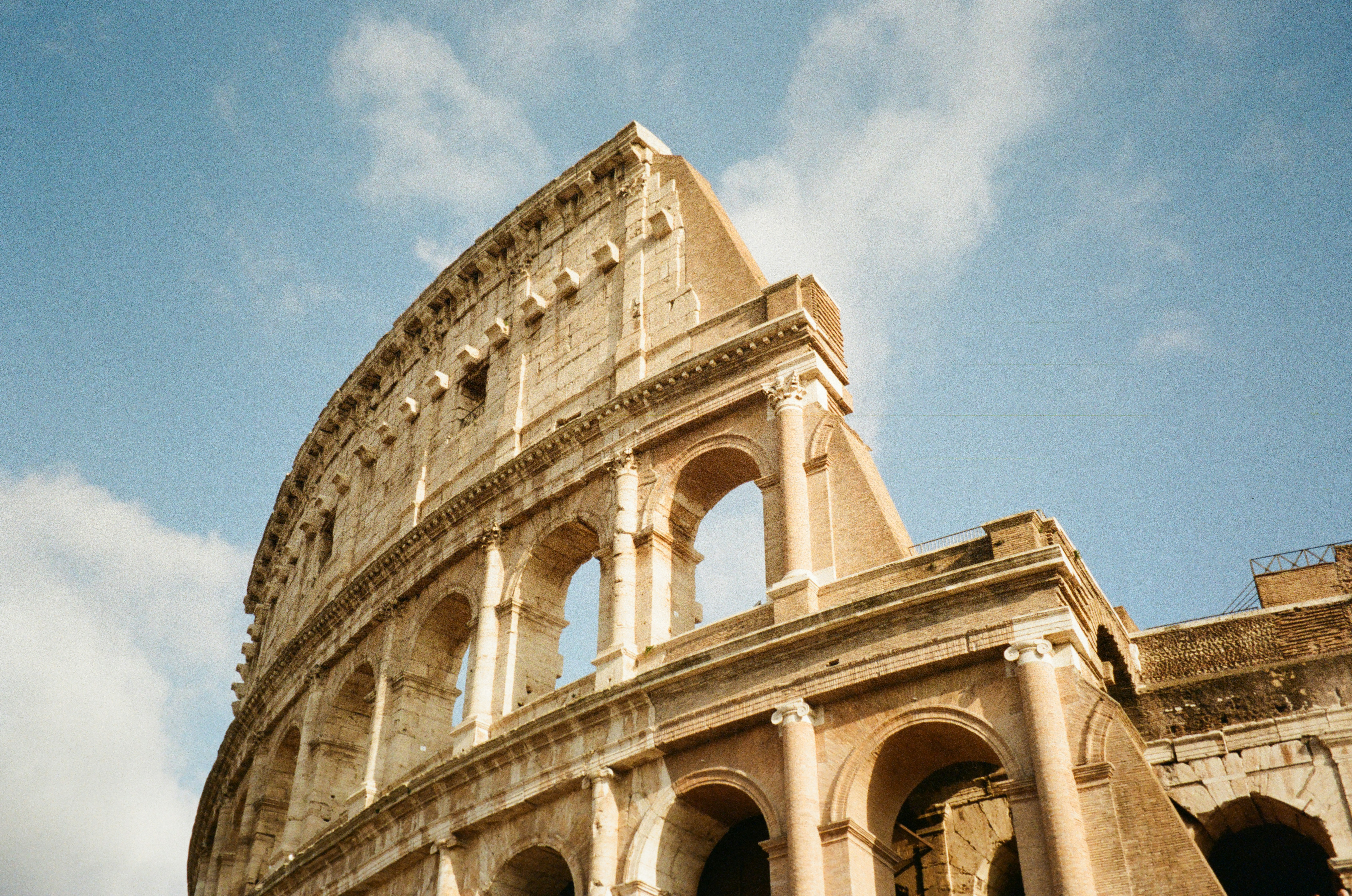 Close-up view of the upper arches and stone facade of the Colosseum in Rome, lit by golden sunlight under a blue sky